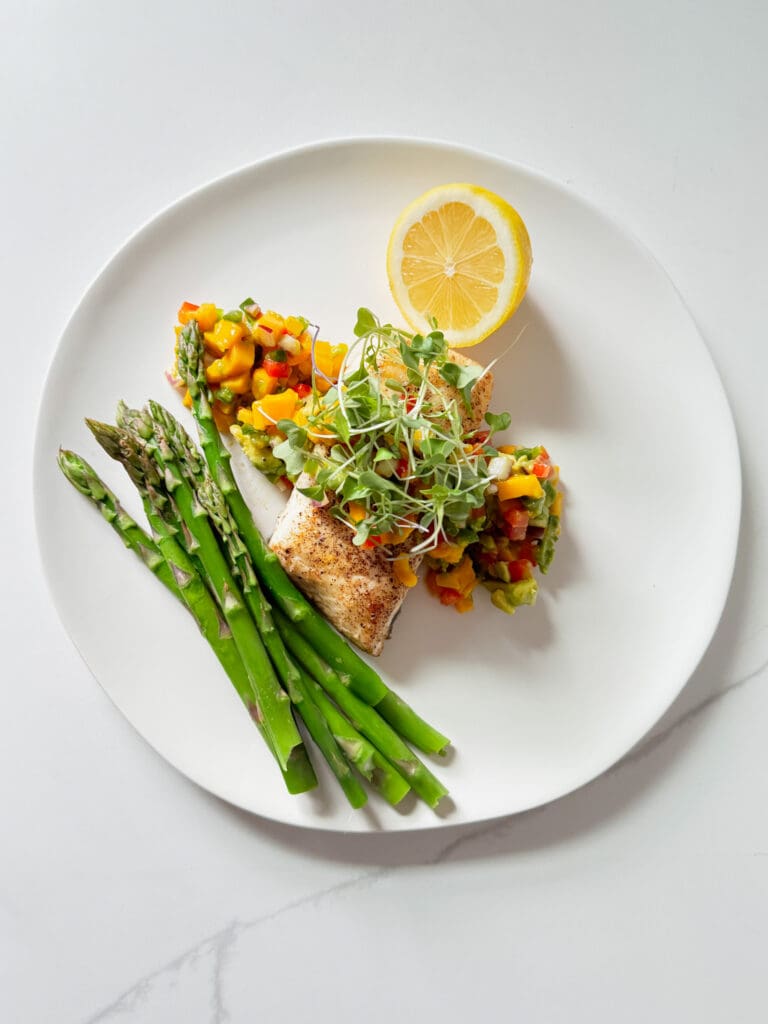pan seared halibut with mango salsa, a lemon and asparagus on a plate