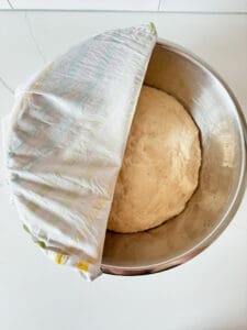 Bagel dough in a bowl with a moist towel over top