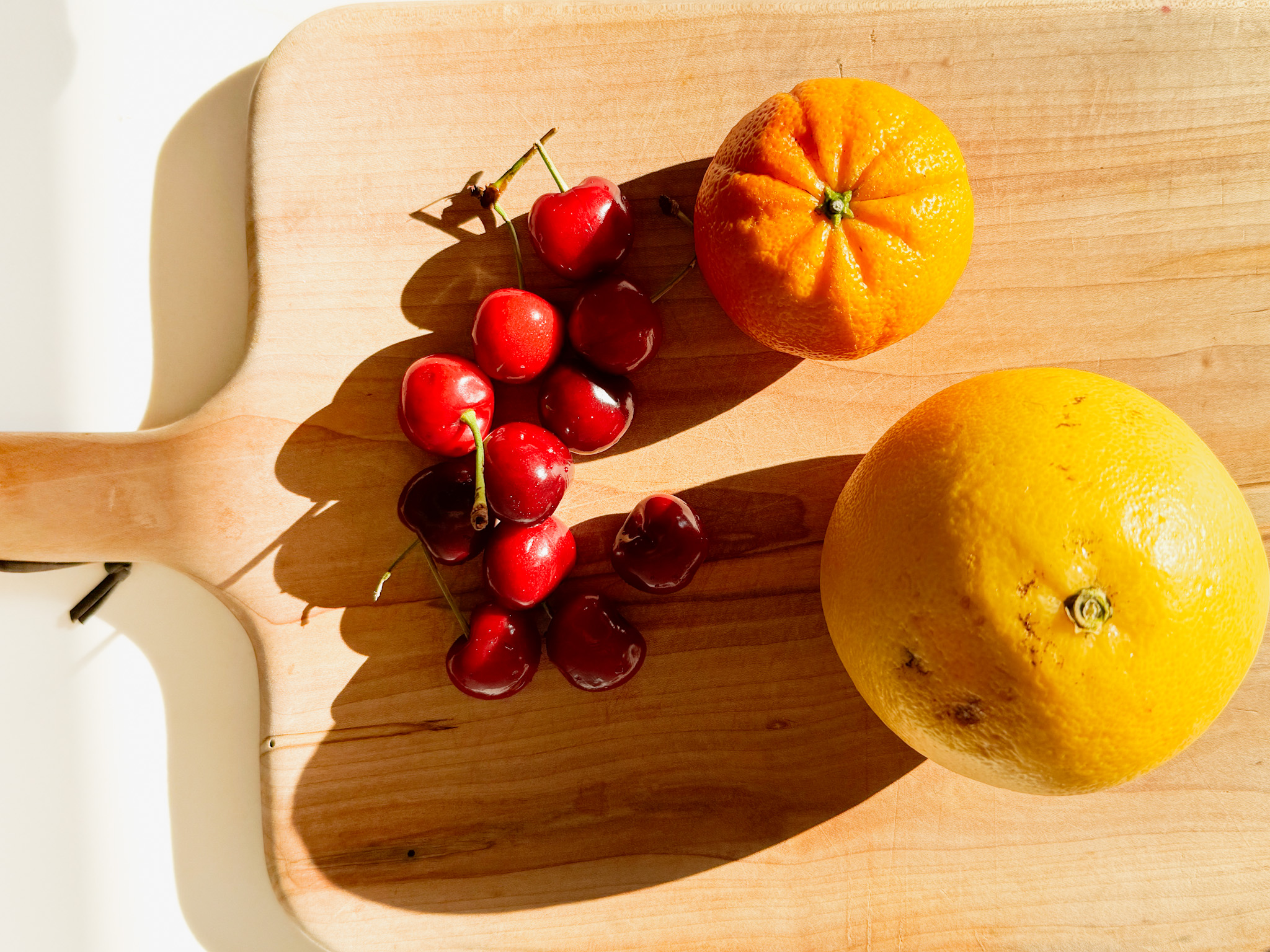 Cutting board with cherries, a grapefruit and a smal orange.
