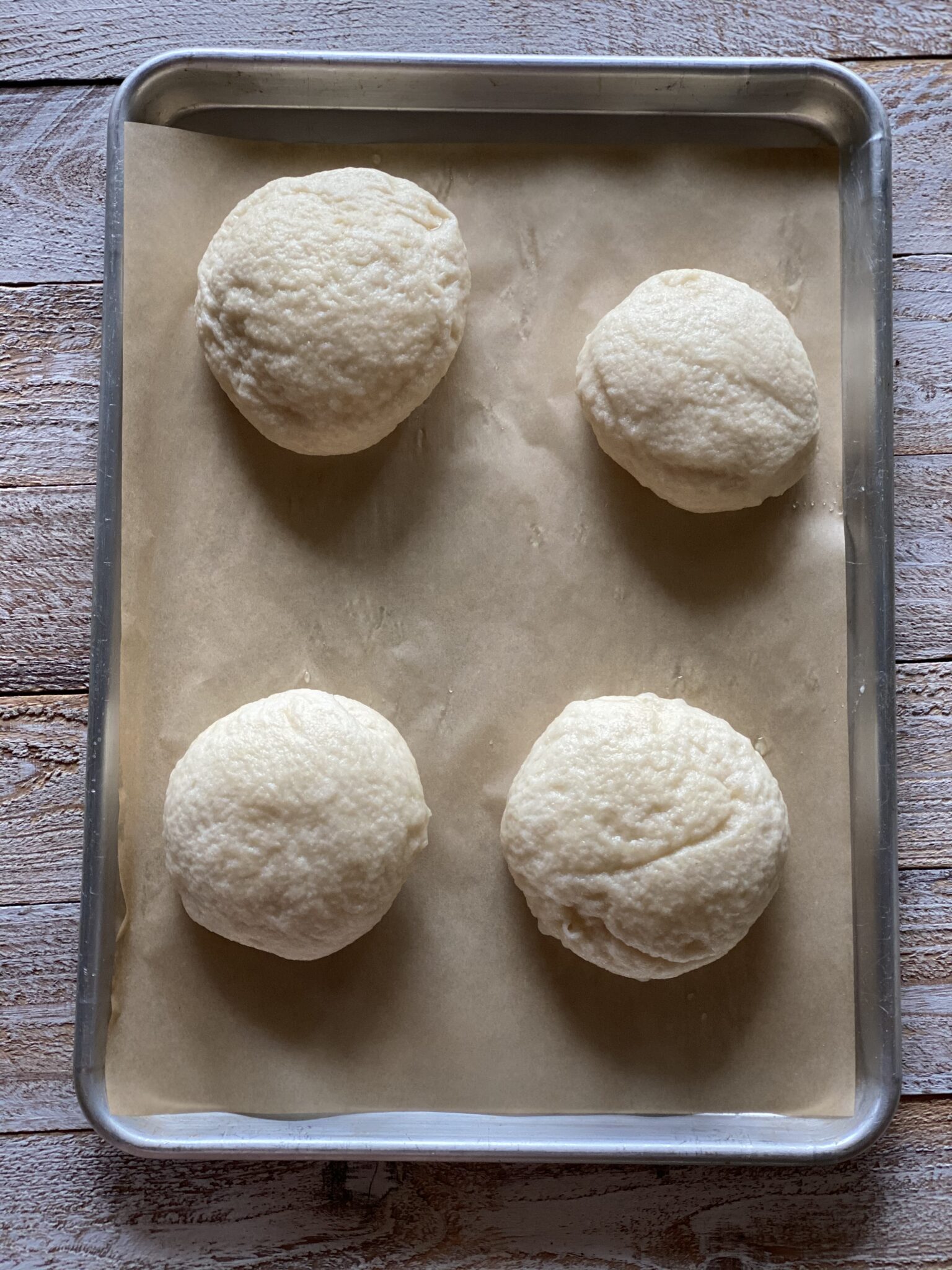 4 pizza dough balls on parchment paper on a cookie sheet