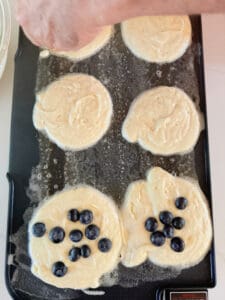 Pancakes on a griddle with blueberries on some