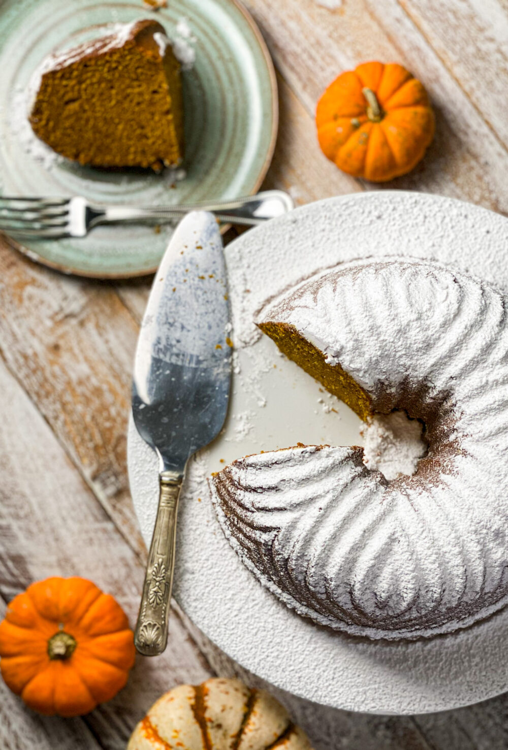 Powder sugar topped pumpkin bundt cake with a slice out and baby pumpkins