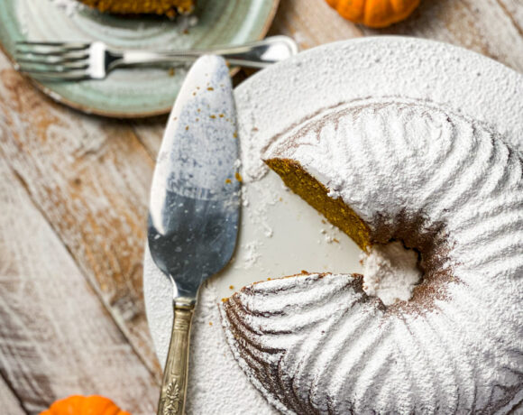 Powder sugar topped pumpkin bundt cake with a slice out and baby pumpkins