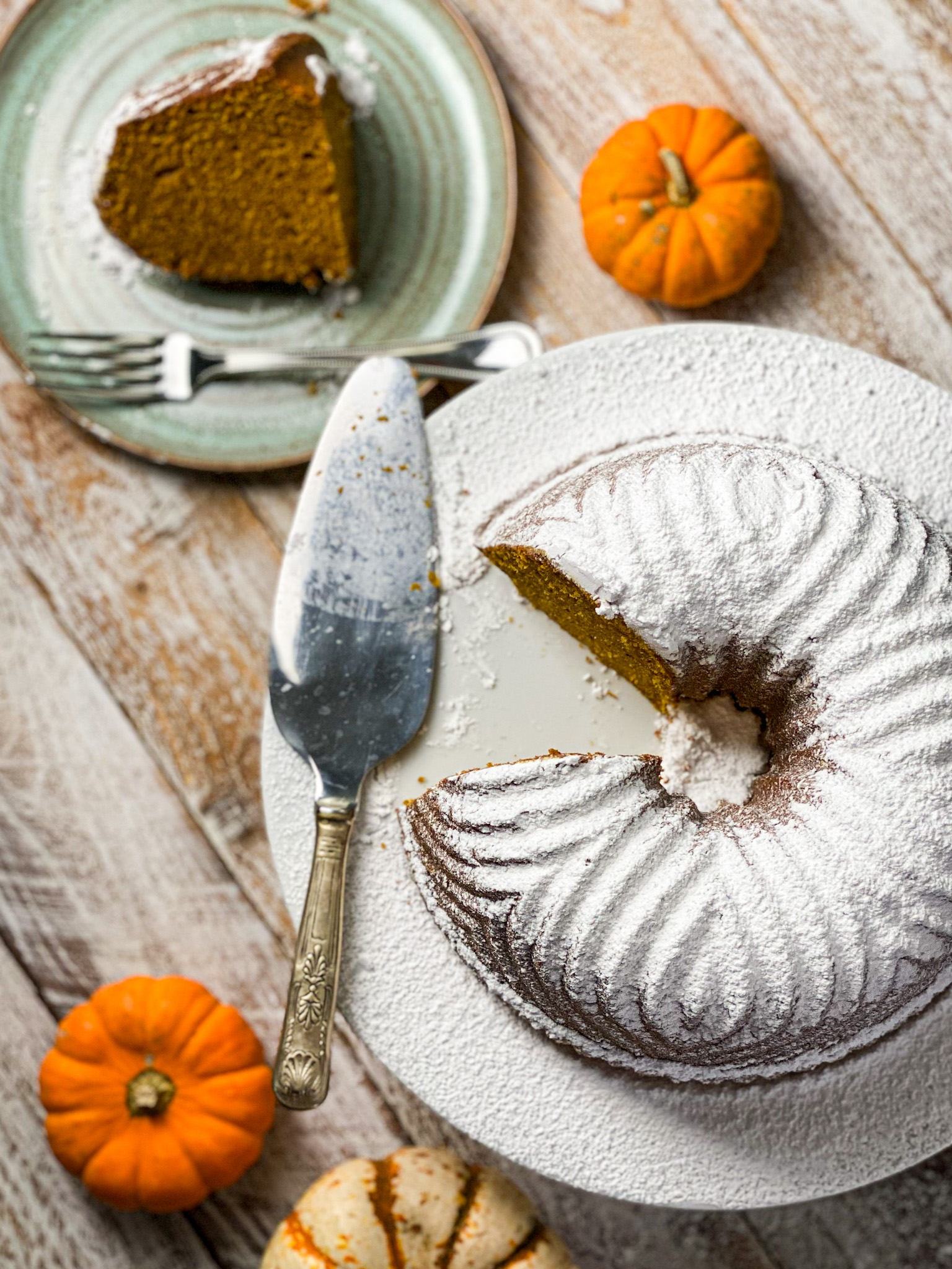 Powder sugar topped pumpkin bundt cake with a slice out and baby pumpkins