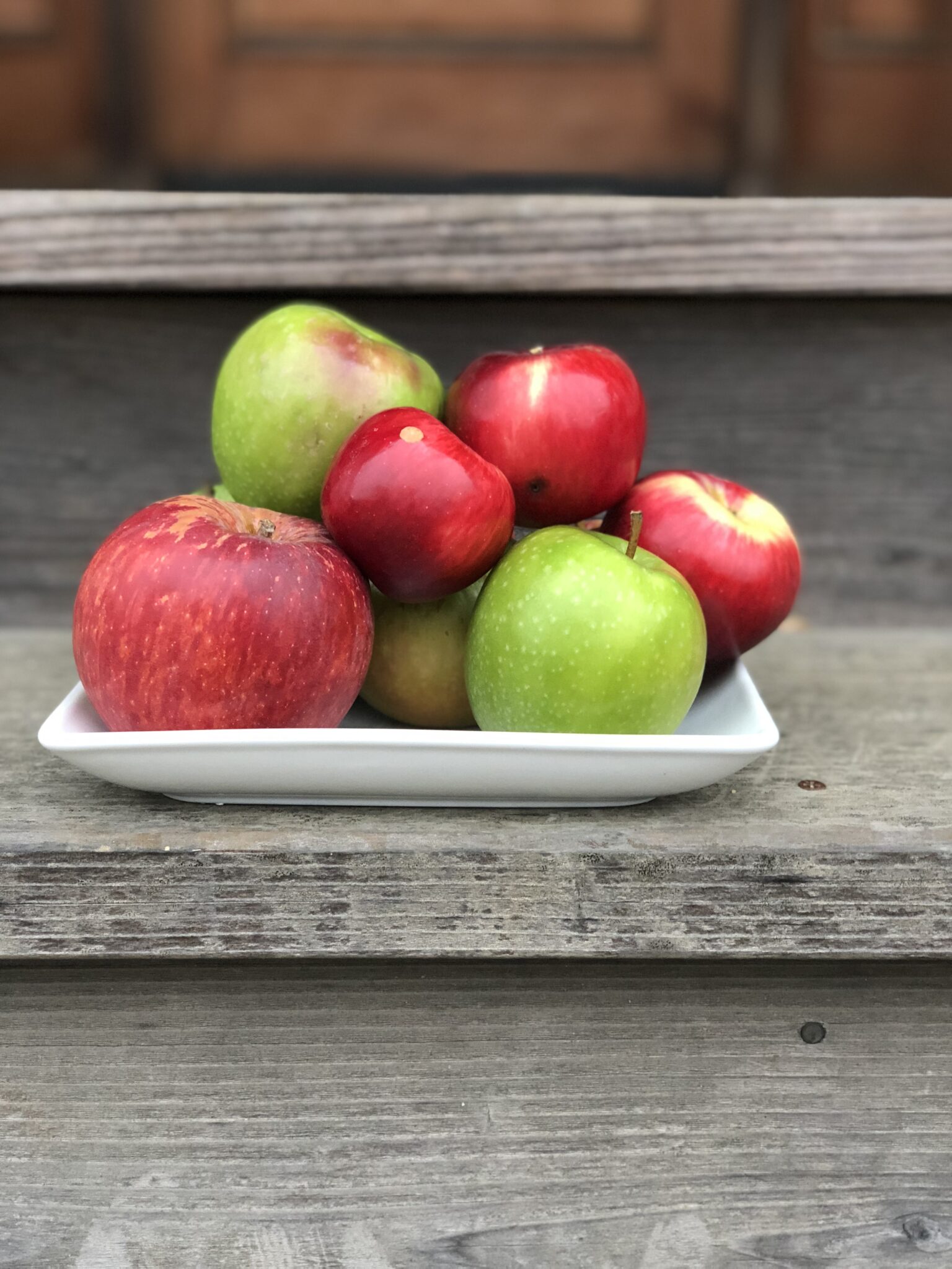 white plate with red and green apples on a step