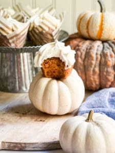 pumpkin cupcake with cream cheese frosting with a bite out of it sitting on a white pumpkin