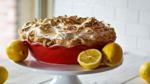Lemon Meringue pie on a white pedastal with 2 lemons
