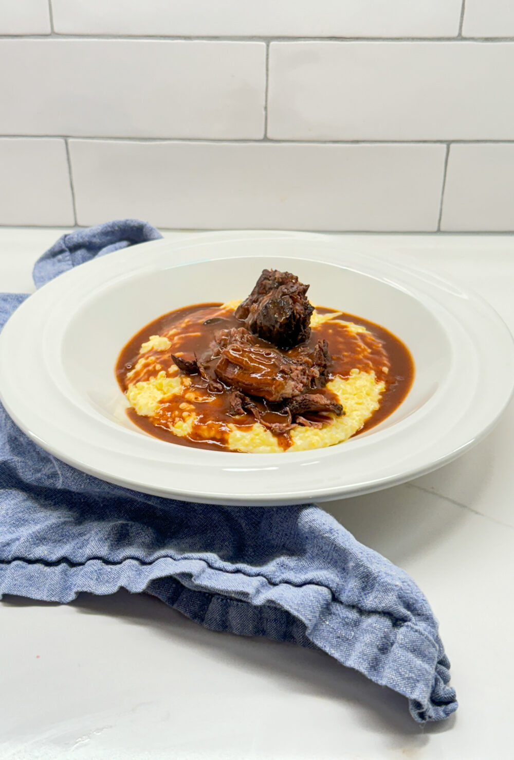 pot roast and gravy on grits in a white bowl with a blue napkin