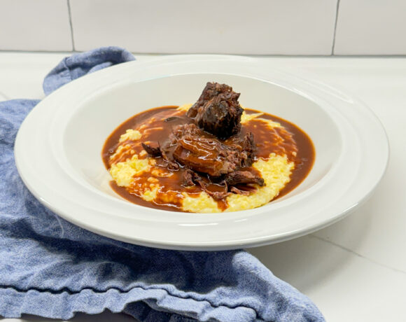 pot roast and gravy on grits in a white bowl with a blue napkin