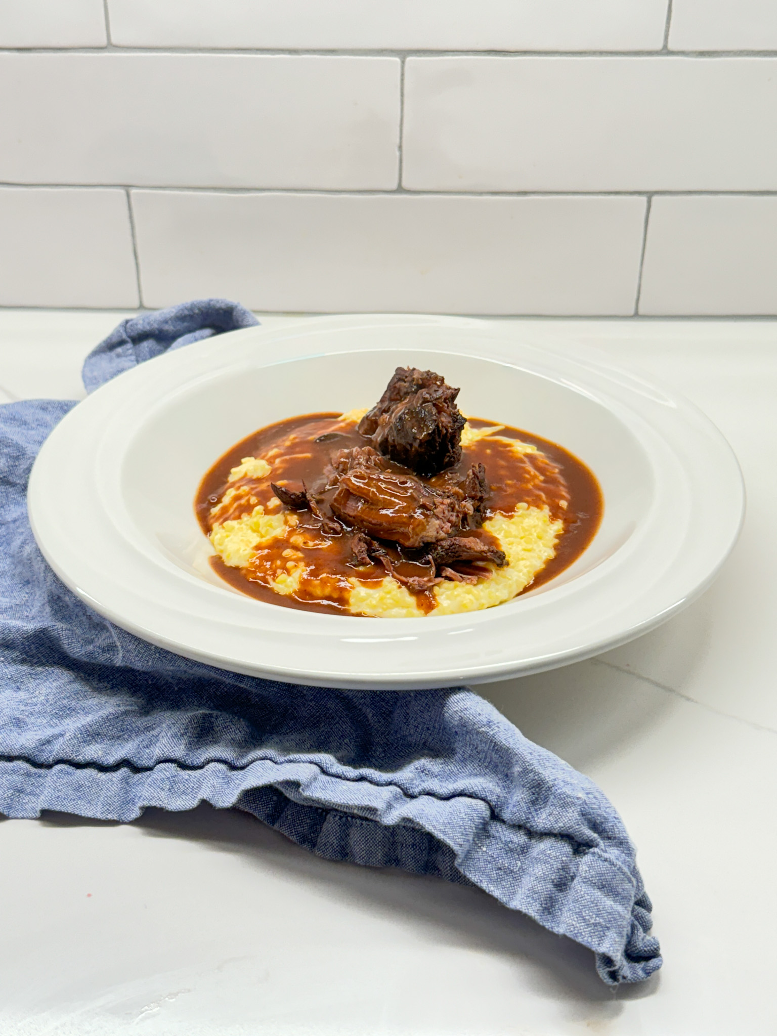 pot roast and gravy on grits in a white bowl with a blue napkin