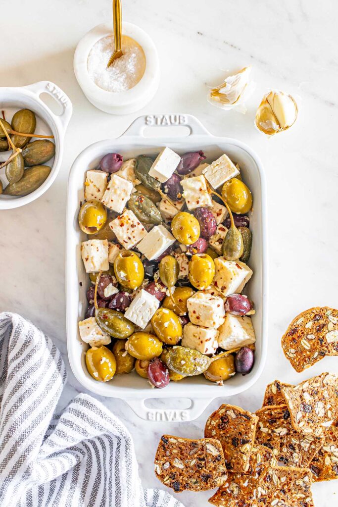 a white Staub pan with marinated olives and feta
