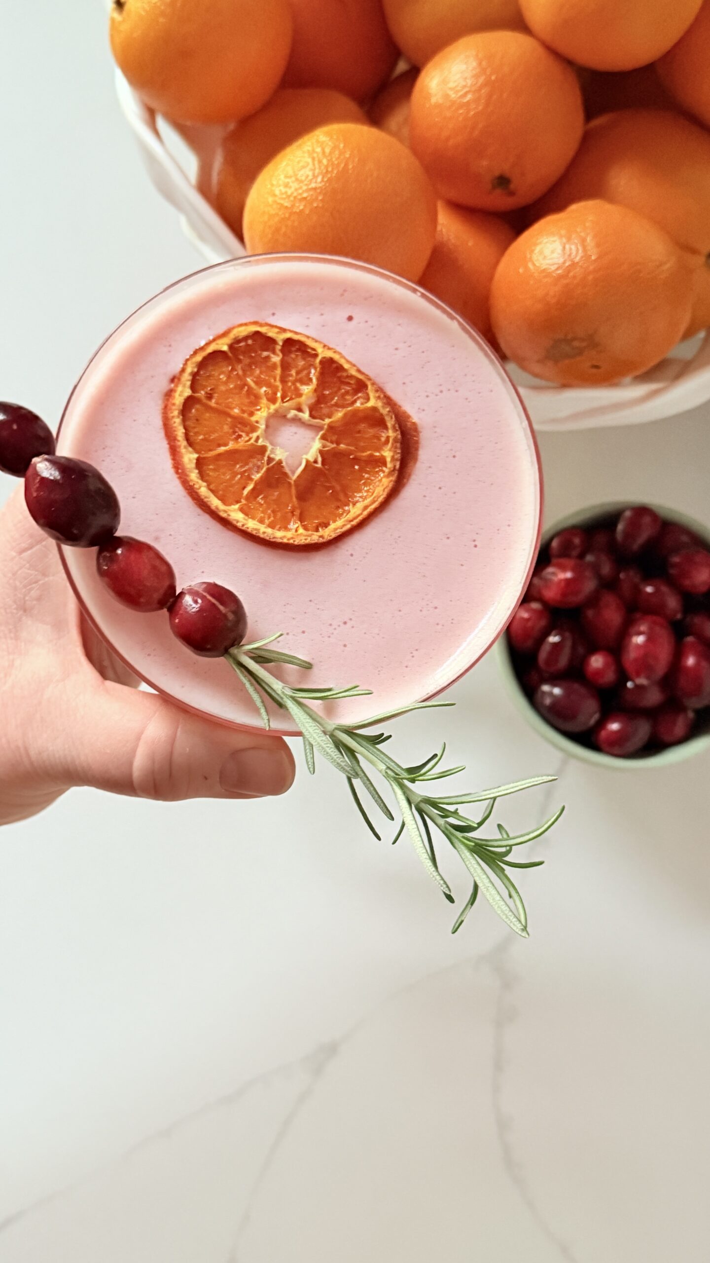 top down cranberry orange whiskey sour with an orange slice and cranberries and rosemar