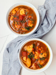 2 bowls of tortellini tomato and kale soup with a blue and white napkin