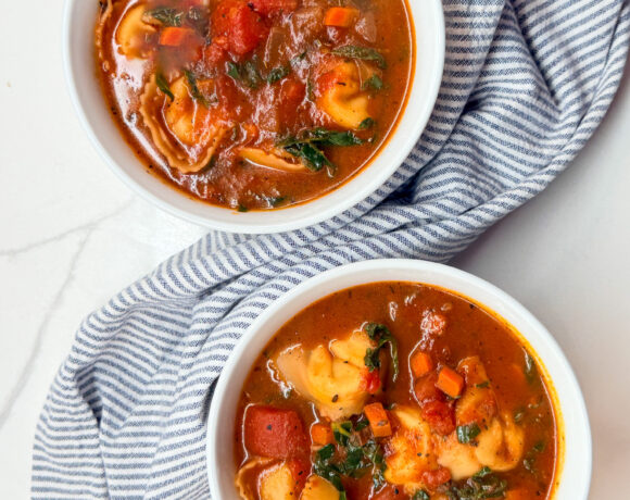 2 bowls of tortellini tomato and kale soup with a blue and white napkin