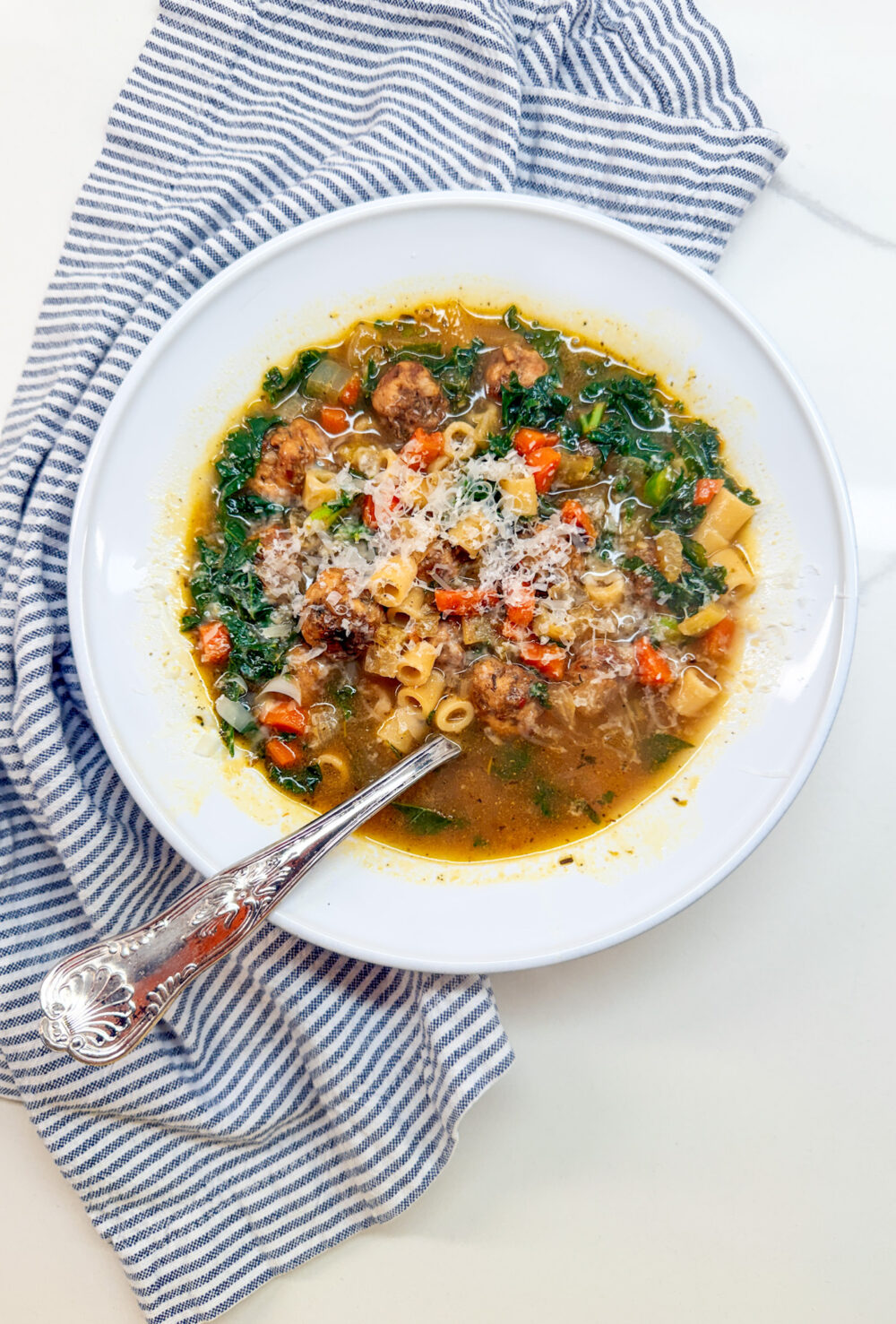 Italian Wedding Soup with meatballs in a white owl with a spoon and a blue and white napking
