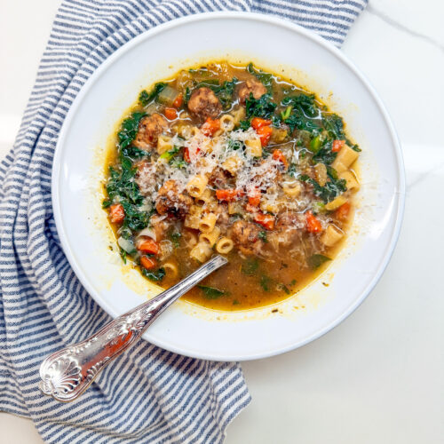 Italian Wedding Soup with meatballs in a white owl with a spoon and a blue and white napking