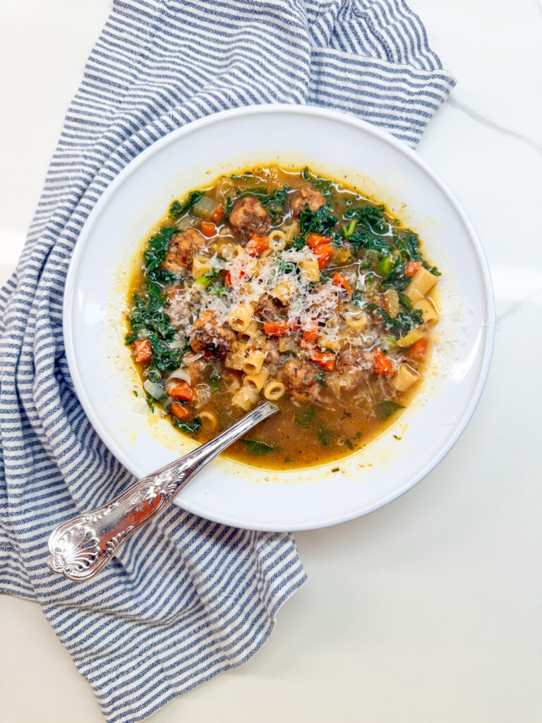 Italian Wedding Soup with meatballs in a white owl with a spoon and a blue and white napking