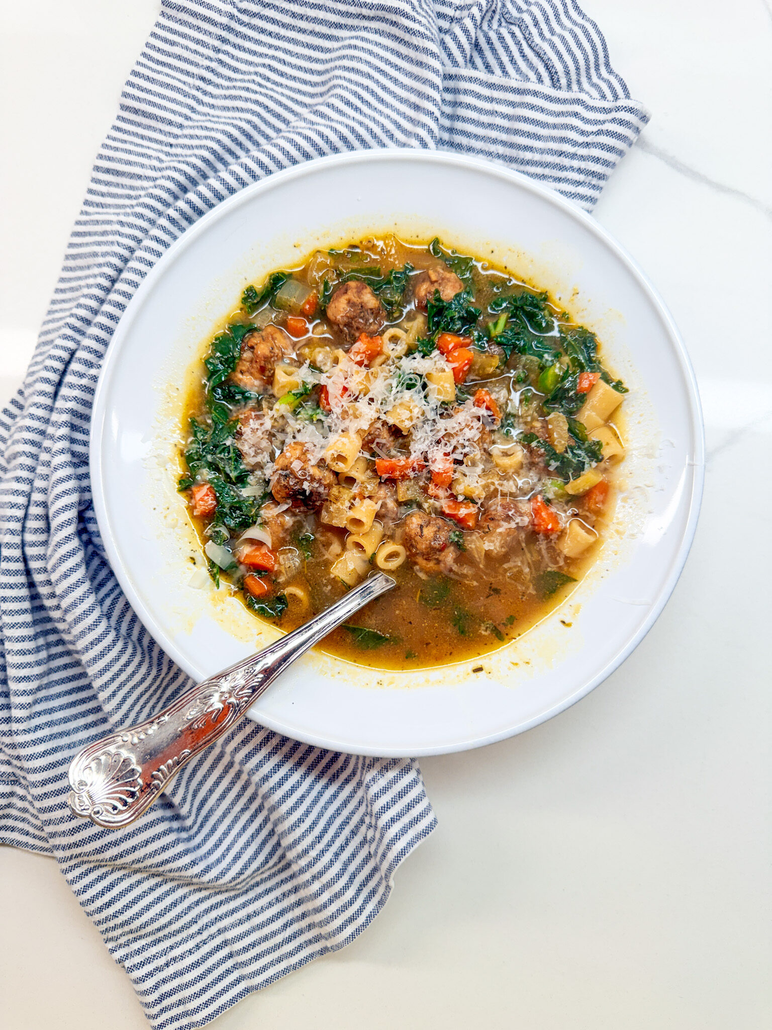 Italian Wedding Soup with meatballs in a white owl with a spoon and a blue and white napking