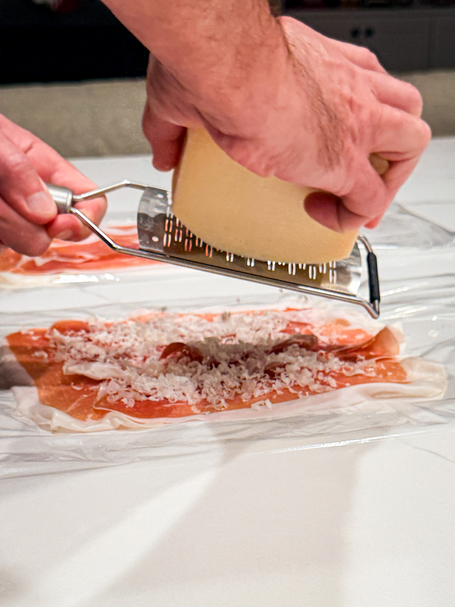 parmesan cheese being grated on prosciuotto
